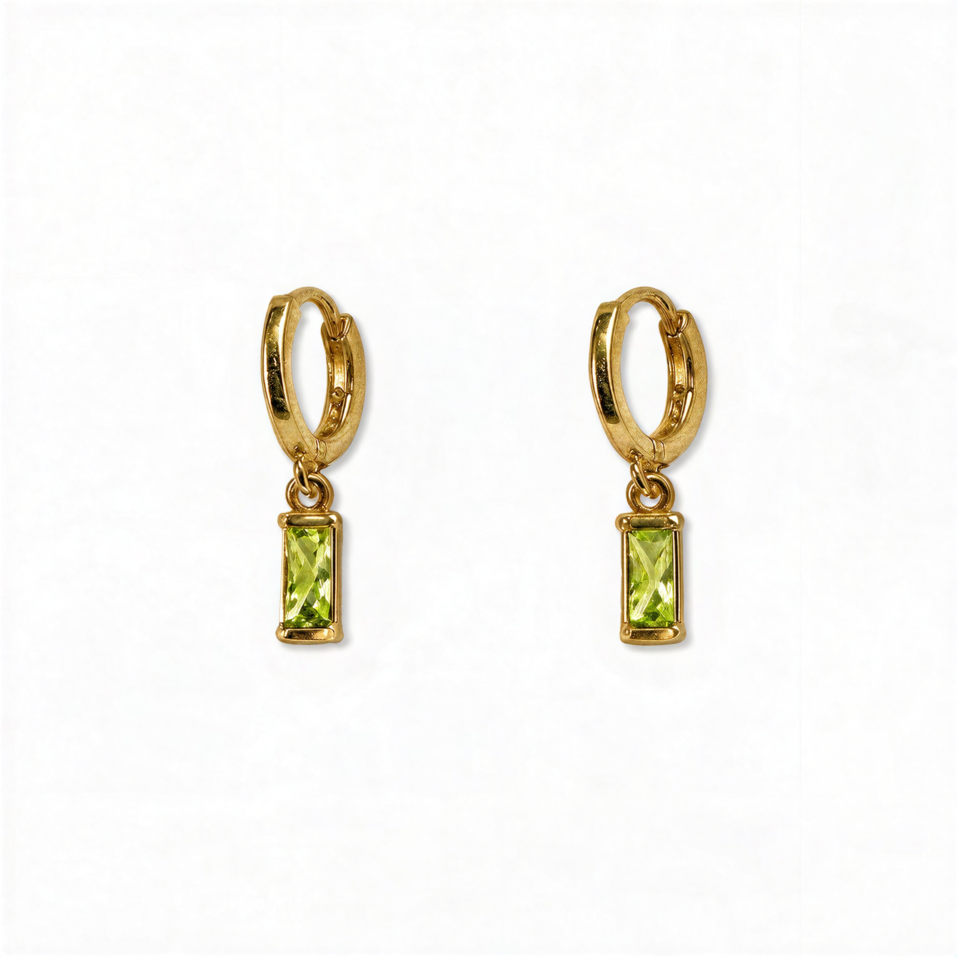 A pair of August Birthstone Peridot Cubic Zirconia Baguette Earrings by Skōsh Jewelry, featuring small gold huggie hoops, each with a rectangular light green baguette stone dangling below, displayed against a white background.