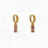 A pair of October Birthstone Pink Cubic Zirconia Baguette Earrings by Skōsh Jewelry, featuring small gold huggie hoops, each with a rectangular pink baguette stone dangling below, displayed against a white background.