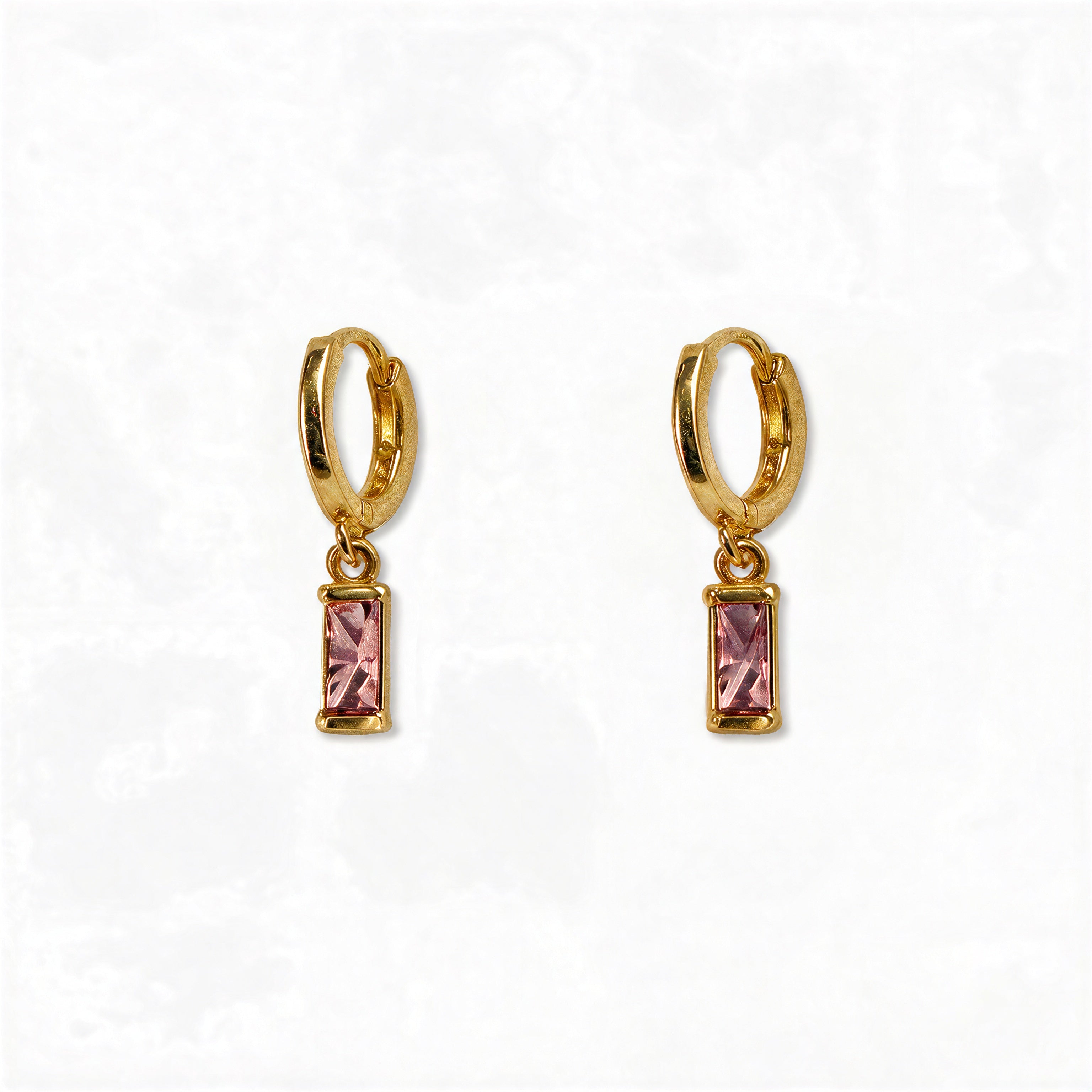 A pair of October Birthstone Pink Cubic Zirconia Baguette Earrings by Skōsh Jewelry, featuring small gold huggie hoops, each with a rectangular pink baguette stone dangling below, displayed against a white background.