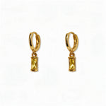 A pair of November Birthstone Citrine Cubic Zirconia Baguette Earrings by Skōsh Jewelry, featuring small gold huggie hoops, each with a rectangular yellow baguette stone dangling below, displayed against a white background.