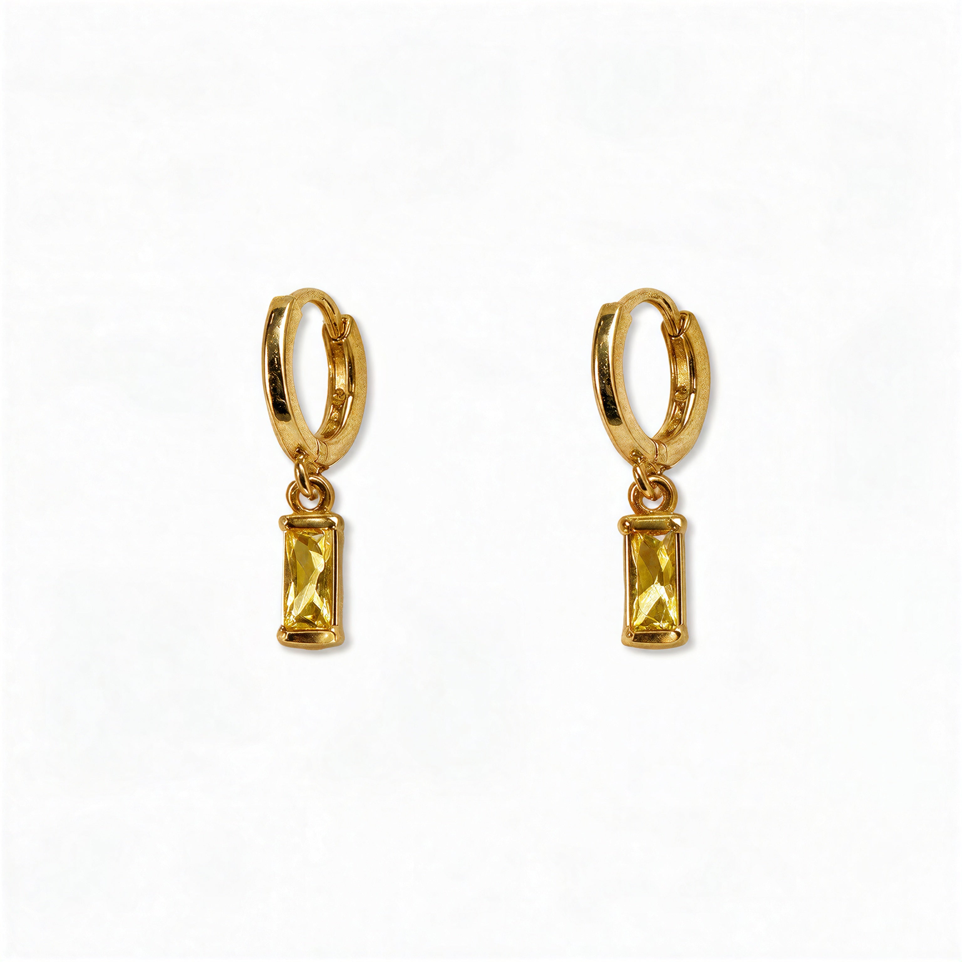 A pair of November Birthstone Citrine Cubic Zirconia Baguette Earrings by Skōsh Jewelry, featuring small gold huggie hoops, each with a rectangular yellow baguette stone dangling below, displayed against a white background.