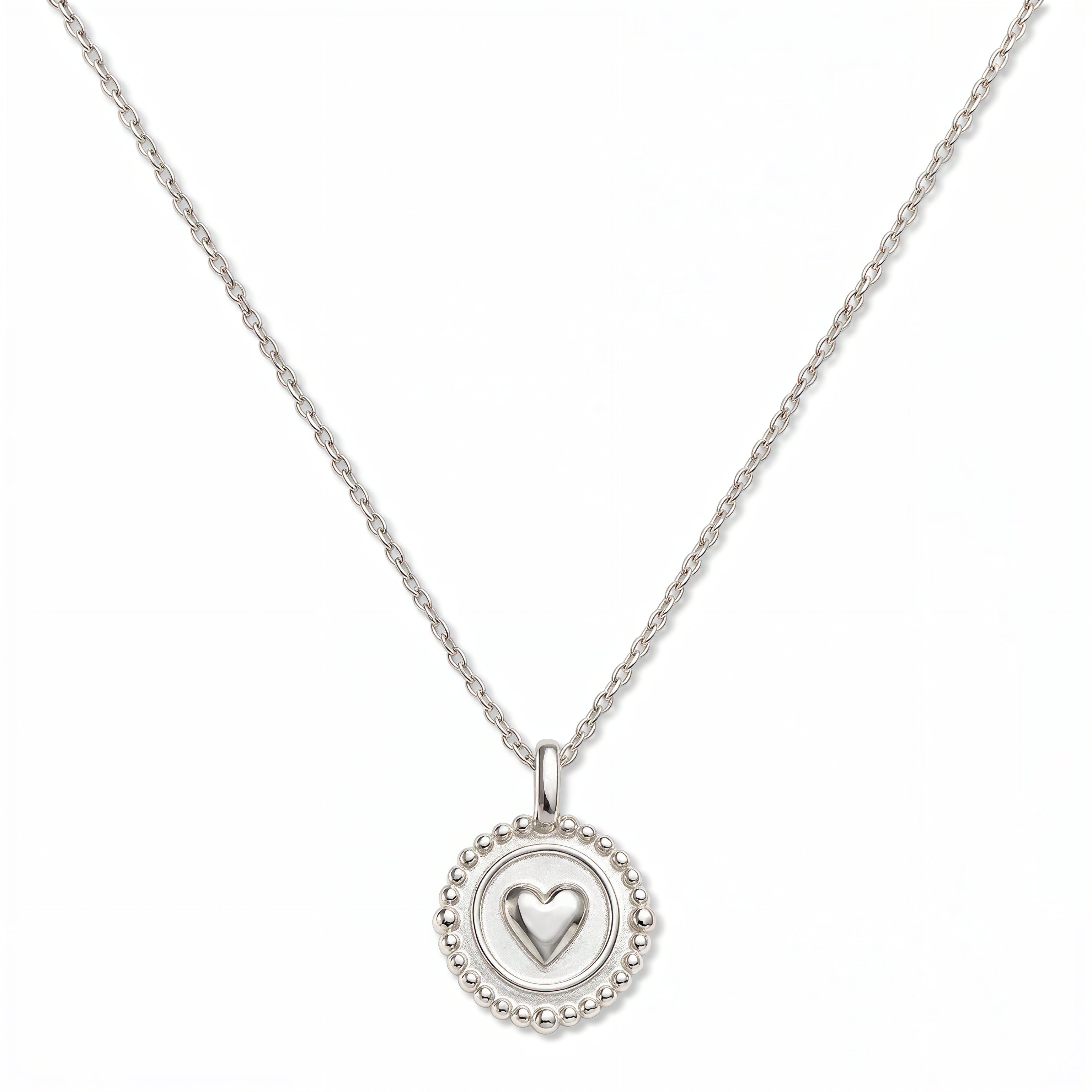 A Pass Love Along Heart Disc Pendant Necklace by Skōsh Jewelry, featuring a round medallion with a raised heart at its center framed by a beaded border on a fine sterling silver chain, displayed against a white background.