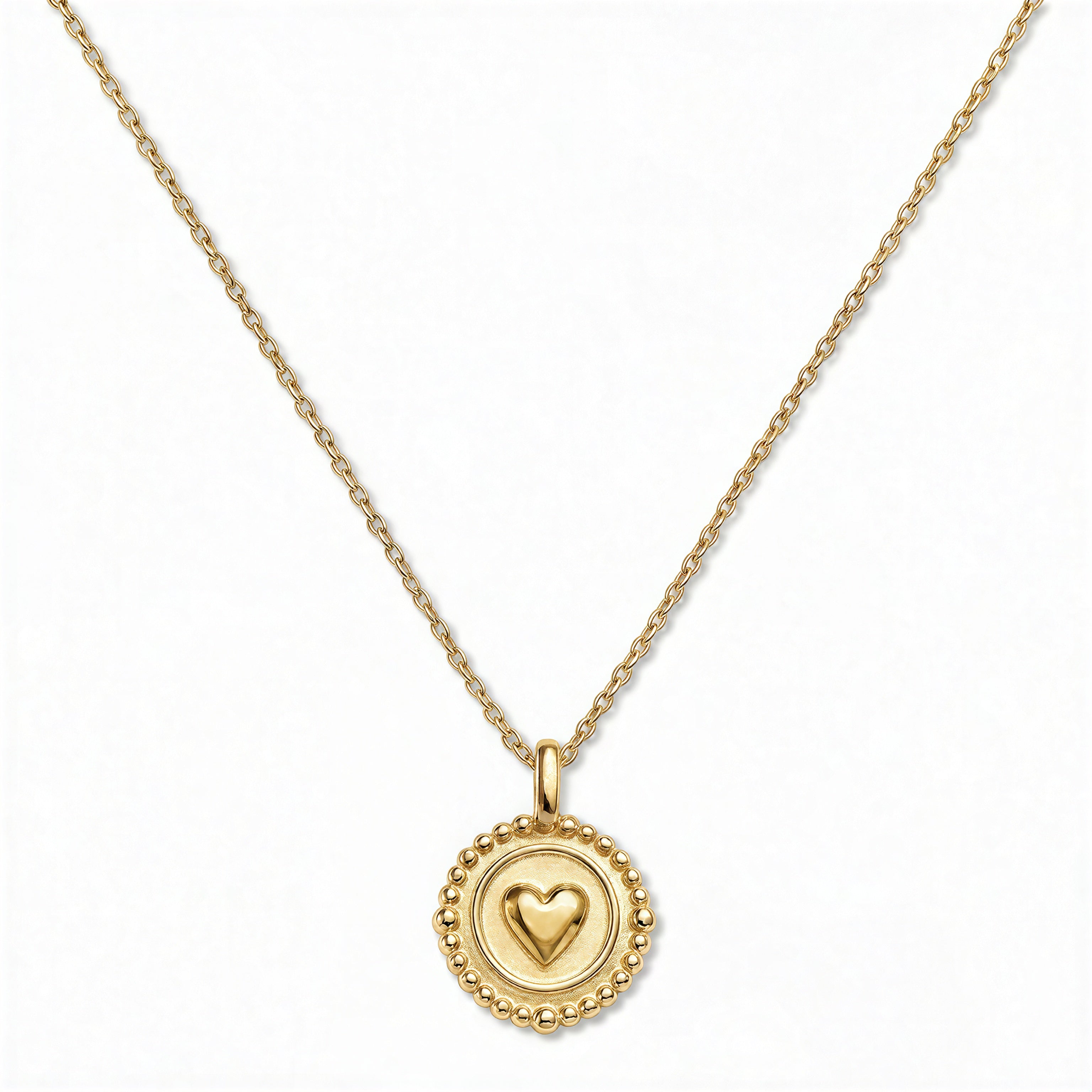 A Pass Love Along Heart Disc Pendant Necklace by Skōsh Jewelry, featuring a round medallion with a raised heart at its center framed by a beaded border on a fine gold chain, displayed against a white background.