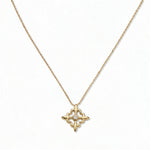 A Louisiana Fleur-de-lis with White Cubic Zirconia Accent Pendant Necklace by Skōsh Jewelry, featuring a fleur-de-lis cross with a small clear stone at its center on a fine gold chain, displayed against a white background.