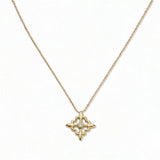 A Louisiana Fleur-de-lis with White Cubic Zirconia Accent Pendant Necklace by Skōsh Jewelry, featuring a fleur-de-lis cross with a small clear stone at its center on a fine gold chain, displayed against a white background.