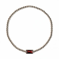 A January Birthstone Garnet Cubic Zirconia Baguette Bracelet by Skōsh Jewelry, featuring a strand of polished sterling silver beads on a stretch cord with a rectangular deep red baguette stone at the center, displayed against a white background.