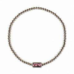 An October Birthstone Pink Cubic Zirconia Baguette Bracelet by Skōsh Jewelry, featuring a strand of polished sterling silver beads on a stretch cord with a rectangular pink baguette stone at the center, displayed against a white background.