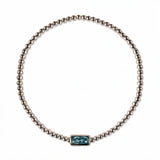 A March Birthstone Light Sapphire Cubic Zirconia Baguette Bracelet by Skōsh Jewelry, featuring a strand of polished sterling silver beads on a stretch cord with a rectangular light blue baguette stone at the center, displayed against a white background.