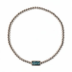 A March Birthstone Light Sapphire Cubic Zirconia Baguette Bracelet by Skōsh Jewelry, featuring a strand of polished sterling silver beads on a stretch cord with a rectangular light blue baguette stone at the center, displayed against a white background.