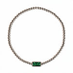 A May Birthstone Emerald Cubic Zirconia Baguette Bracelet by Skōsh Jewelry, featuring a strand of polished sterling silver beads on a stretch cord with a rectangular green baguette stone at the center, displayed against a white background.
