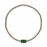 A May Birthstone Emerald Cubic Zirconia Baguette Bracelet by Skōsh Jewelry, featuring a strand of polished sterling silver beads on a stretch cord with a rectangular green baguette stone at the center, displayed against a white background.