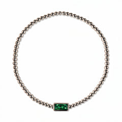 A May Birthstone Emerald Cubic Zirconia Baguette Bracelet by Skōsh Jewelry, featuring a strand of polished sterling silver beads on a stretch cord with a rectangular green baguette stone at the center, displayed against a white background.