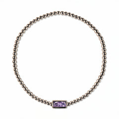 A June Birthstone Lavender Cubic Zirconia Baguette Bracelet by Skōsh Jewelry, featuring a strand of polished sterling silver beads on a stretch cord with a rectangular light purple baguette stone at the center, displayed against a white background.