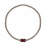 A July Birthstone Ruby Cubic Zirconia Baguette Bracelet by Skōsh Jewelry, featuring a strand of polished sterling silver beads on a stretch cord with a rectangular red baguette stone at the center, displayed against a white background.