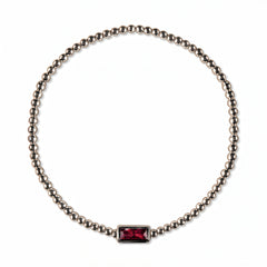 A July Birthstone Ruby Cubic Zirconia Baguette Bracelet by Skōsh Jewelry, featuring a strand of polished sterling silver beads on a stretch cord with a rectangular red baguette stone at the center, displayed against a white background.