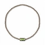 An August Birthstone Peridot Cubic Zirconia Baguette Bracelet by Skōsh Jewelry, featuring a strand of polished sterling silver beads on a stretch cord with a rectangular light green baguette stone at the center, displayed against a white background.