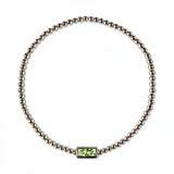 An August Birthstone Peridot Cubic Zirconia Baguette Bracelet by Skōsh Jewelry, featuring a strand of polished sterling silver beads on a stretch cord with a rectangular light green baguette stone at the center, displayed against a white background.