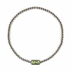 An August Birthstone Peridot Cubic Zirconia Baguette Bracelet by Skōsh Jewelry, featuring a strand of polished sterling silver beads on a stretch cord with a rectangular light green baguette stone at the center, displayed against a white background.