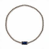 A September Birthstone Sapphire Cubic Zirconia Baguette Bracelet by Skōsh Jewelry, featuring a strand of polished sterling silver beads on a stretch cord with a rectangular deep blue baguette stone at the center, displayed against a white background.