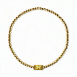 A November Birthstone Citrine Cubic Zirconia Baguette Bracelet by Skōsh Jewelry, featuring a strand of polished gold beads on a stretch cord with a rectangular yellow baguette stone at the center, displayed against a white background.