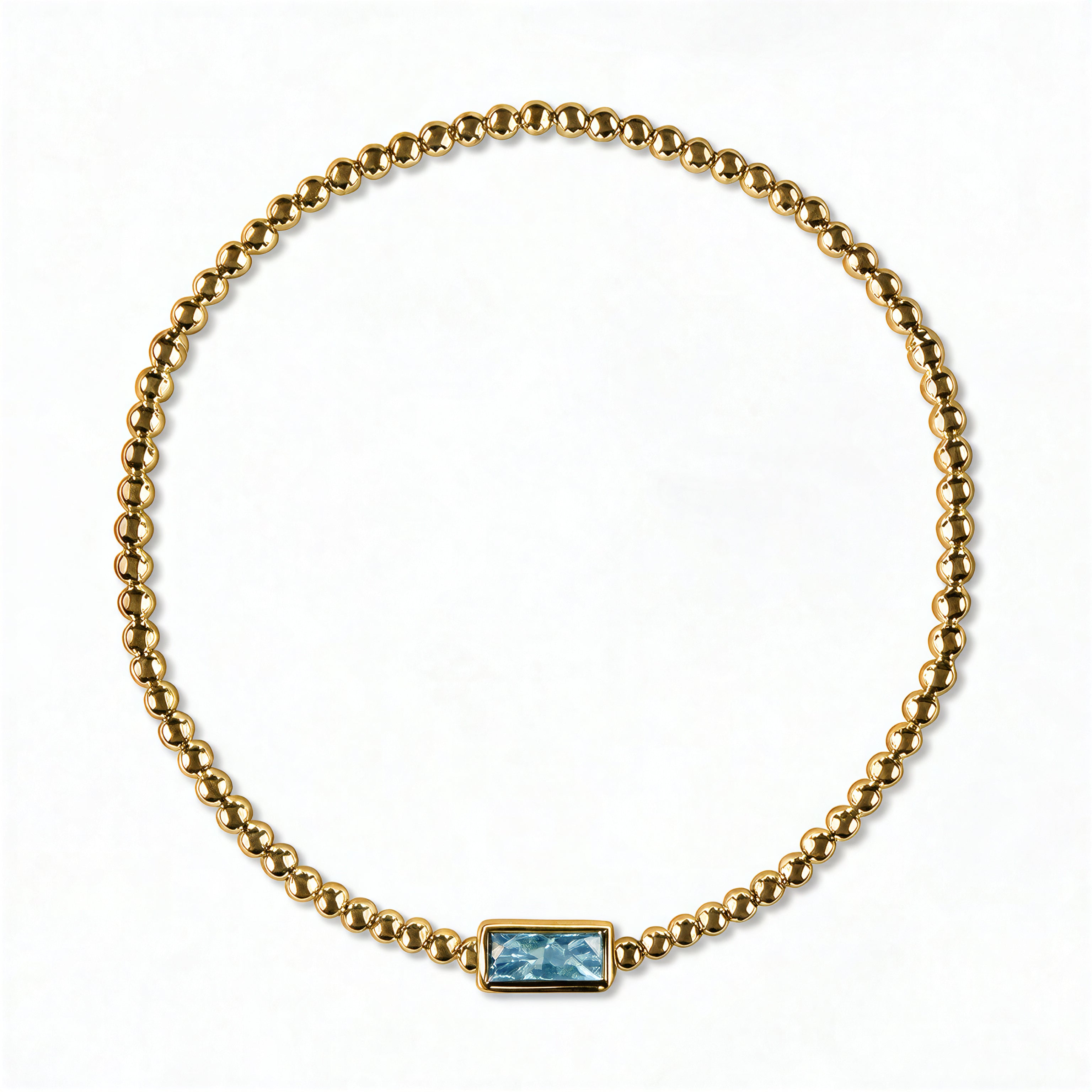 A March Birthstone Light Sapphire Cubic Zirconia Baguette Bracelet by Skōsh Jewelry, featuring a strand of polished gold beads on a stretch cord with a rectangular light blue baguette stone at the center, displayed against a white background.