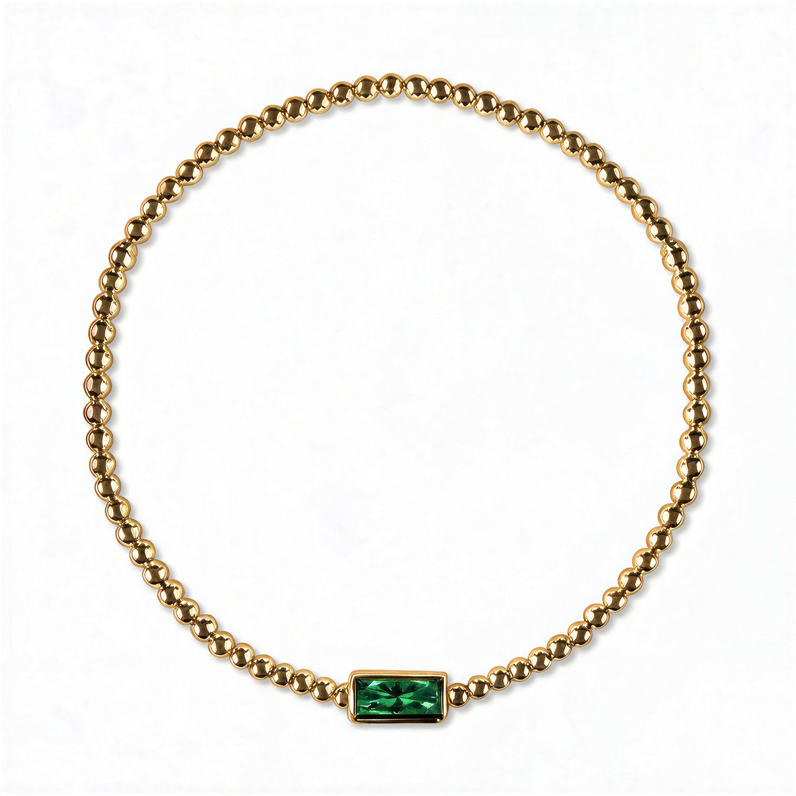 A May Birthstone Emerald Cubic Zirconia Baguette Bracelet by Skōsh Jewelry, featuring a strand of polished gold beads on a stretch cord with a rectangular green baguette stone at the center, displayed against a white background.