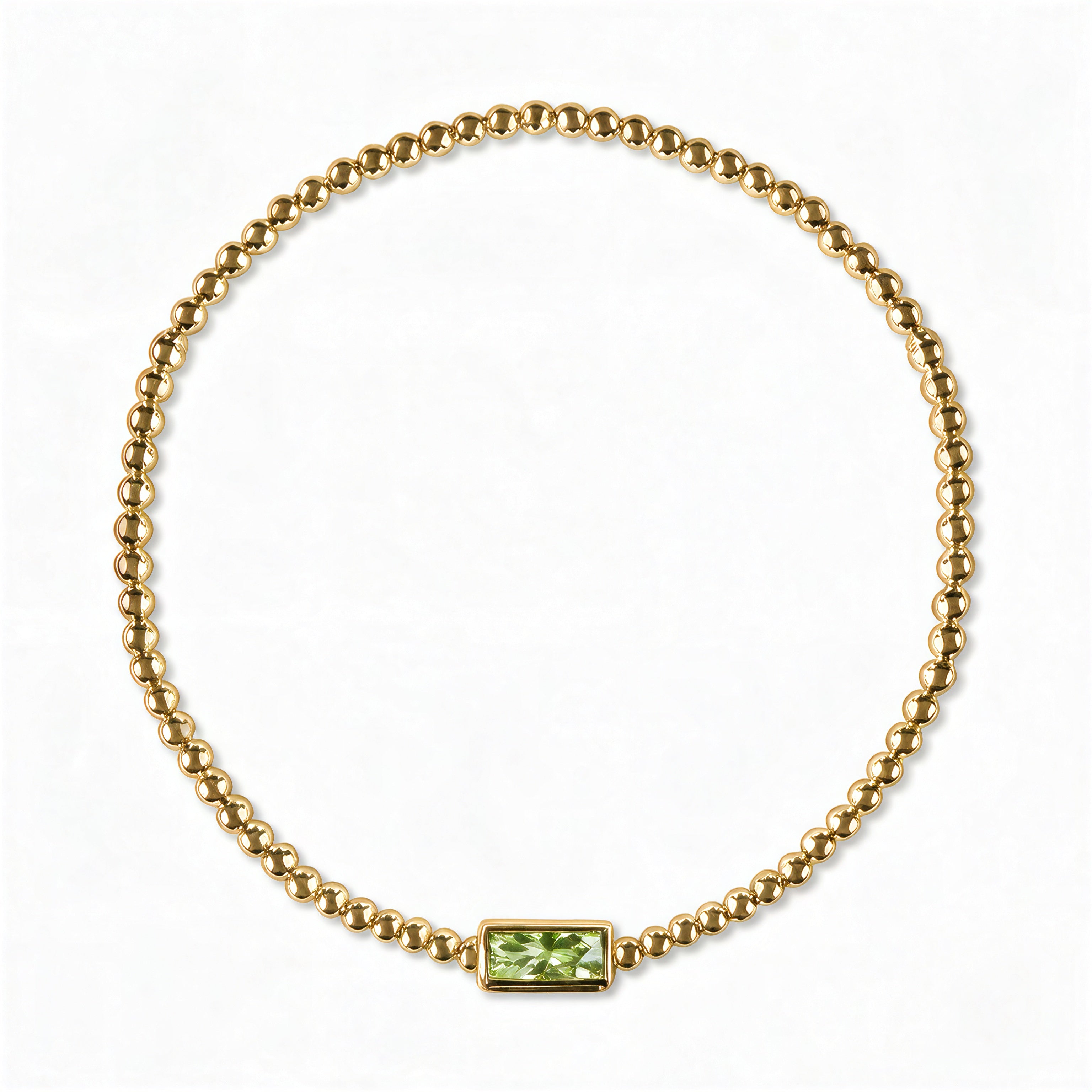 An August Birthstone Peridot Cubic Zirconia Baguette Bracelet by Skōsh Jewelry, featuring a strand of polished gold beads on a stretch cord with a rectangular light green baguette stone at the center, displayed against a white background.