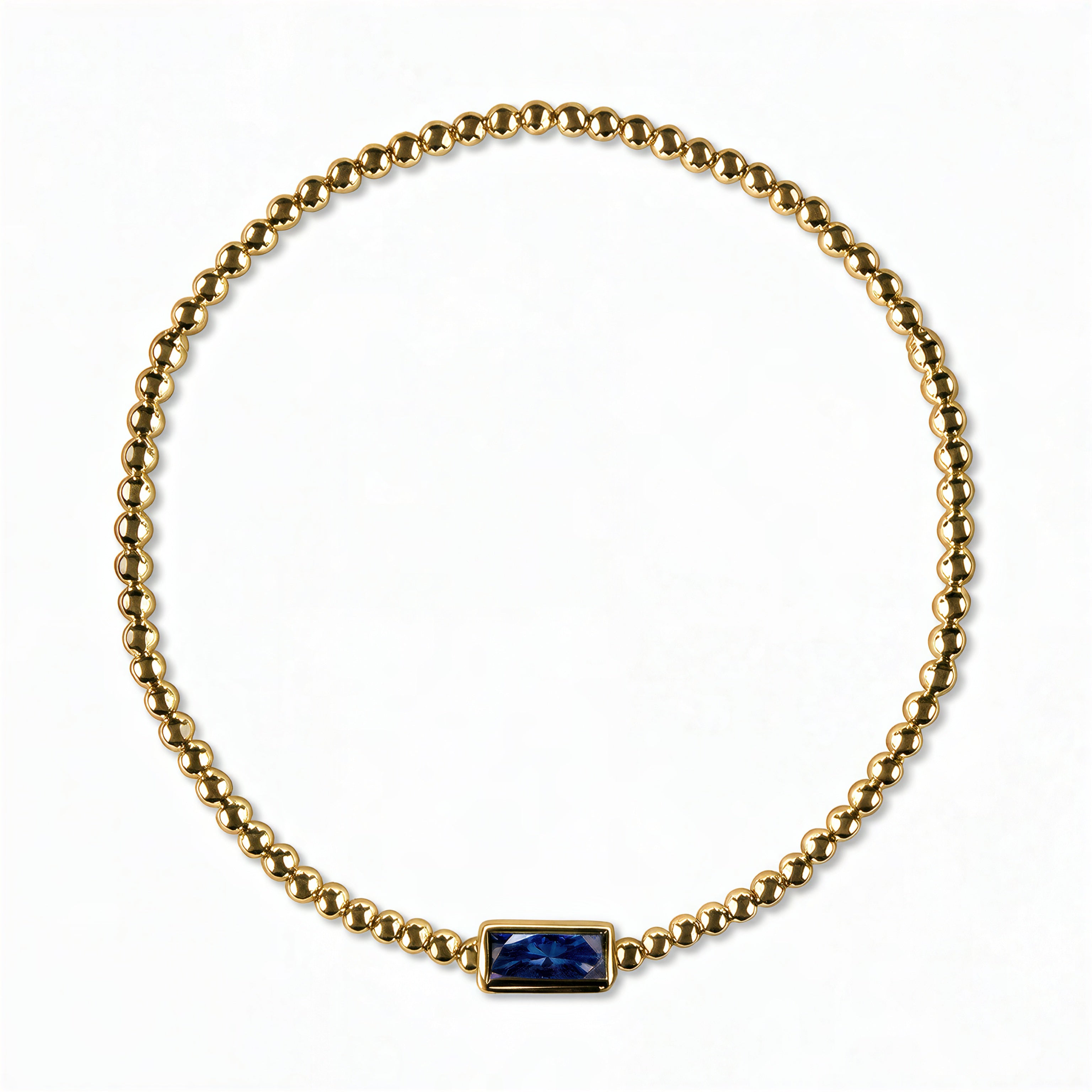 A September Birthstone Sapphire Cubic Zirconia Baguette Bracelet by Skōsh Jewelry, featuring a strand of polished gold beads on a stretch cord with a rectangular deep blue baguette stone at the center, displayed against a white background.