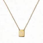 An Engraved Initial Necklace Letter B by Skōsh Jewelry, featuring a small rectangular tag engraved with the letter B on a fine gold chain, displayed against a white background.