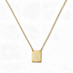An Engraved Initial Necklace Letter D by Skōsh Jewelry, featuring a small rectangular tag engraved with the letter D on a fine gold chain, displayed against a white background.
