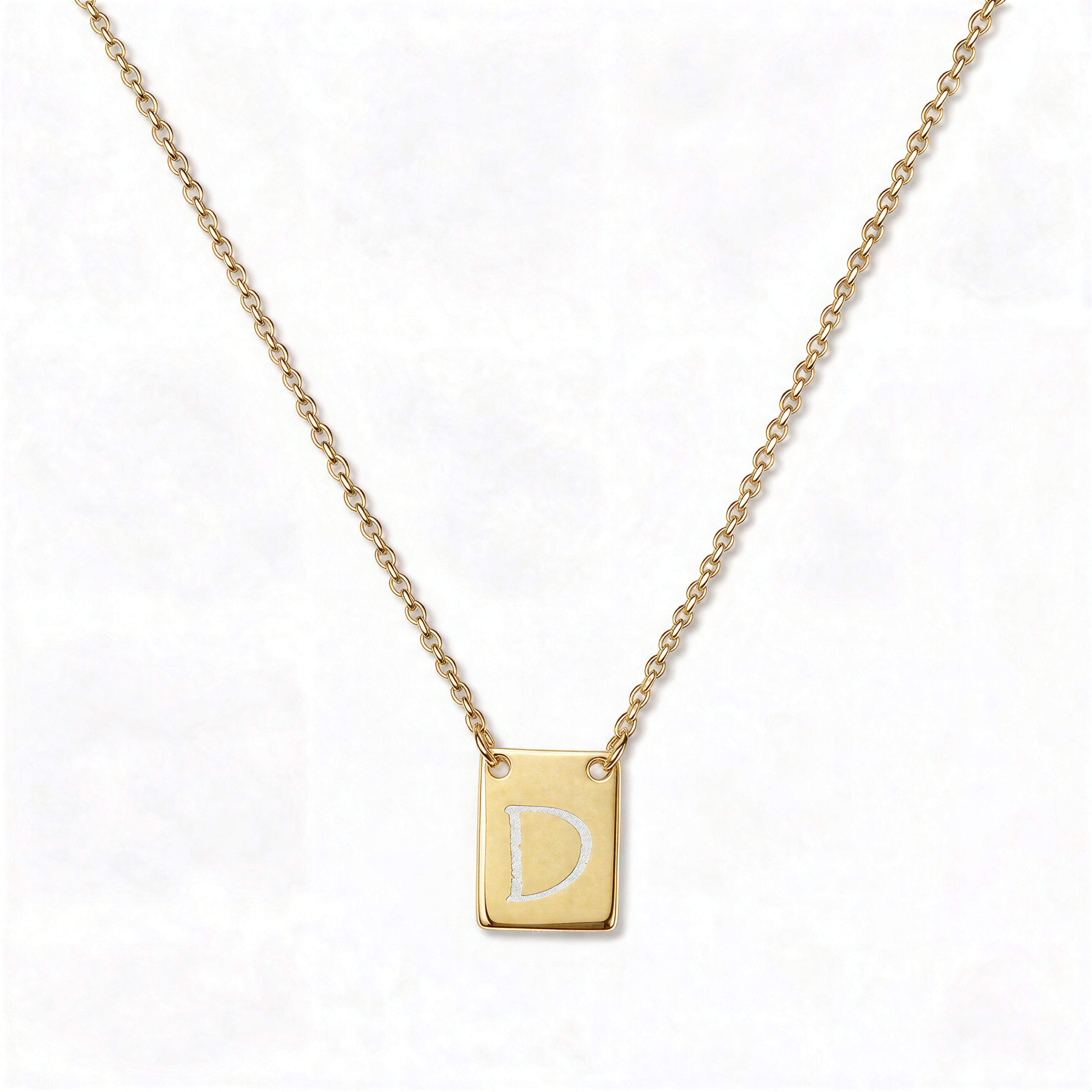 An Engraved Initial Necklace Letter D by Skōsh Jewelry, featuring a small rectangular tag engraved with the letter D on a fine gold chain, displayed against a white background.