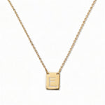 An Engraved Initial Necklace Letter E by Skōsh Jewelry, featuring a small rectangular tag engraved with the letter E on a fine gold chain, displayed against a white background.
