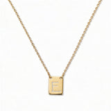 An Engraved Initial Necklace Letter E by Skōsh Jewelry, featuring a small rectangular tag engraved with the letter E on a fine gold chain, displayed against a white background.