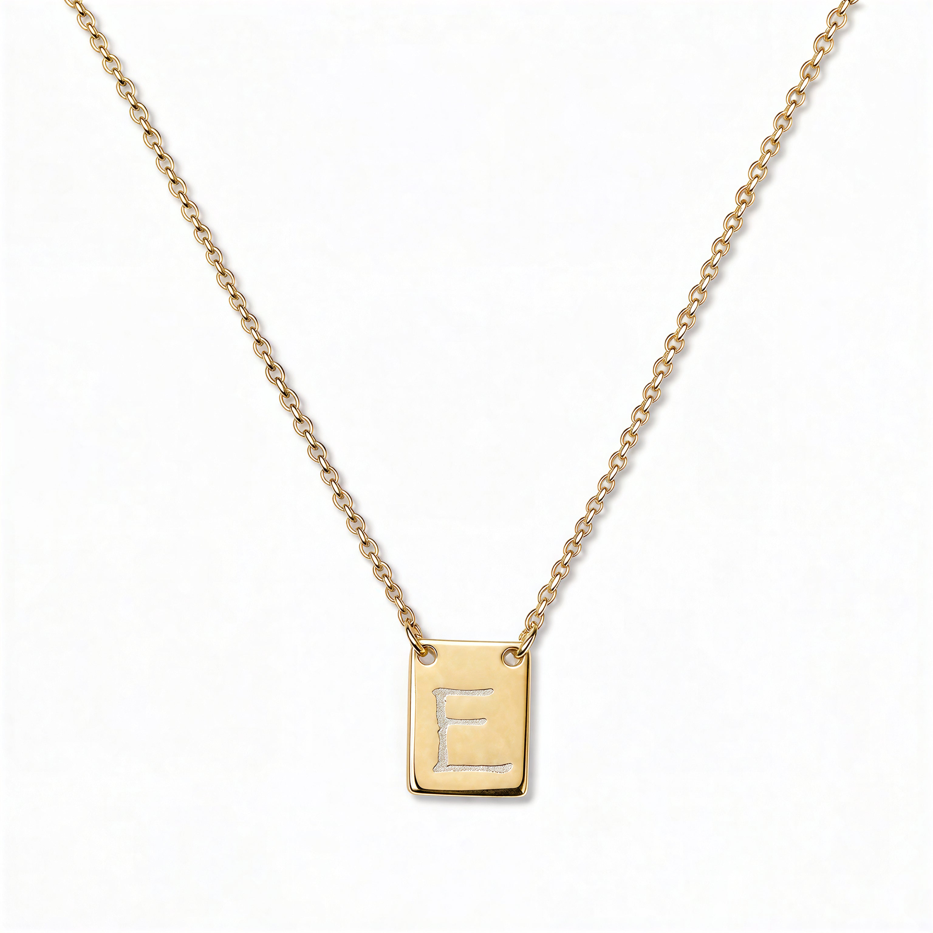 An Engraved Initial Necklace Letter E by Skōsh Jewelry, featuring a small rectangular tag engraved with the letter E on a fine gold chain, displayed against a white background.
