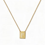 An Engraved Initial Necklace Letter F by Skōsh Jewelry, featuring a small rectangular tag engraved with the letter F on a fine gold chain, displayed against a white background.