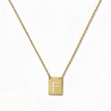 An Engraved Initial Necklace Letter F by Skōsh Jewelry, featuring a small rectangular tag engraved with the letter F on a fine gold chain, displayed against a white background.