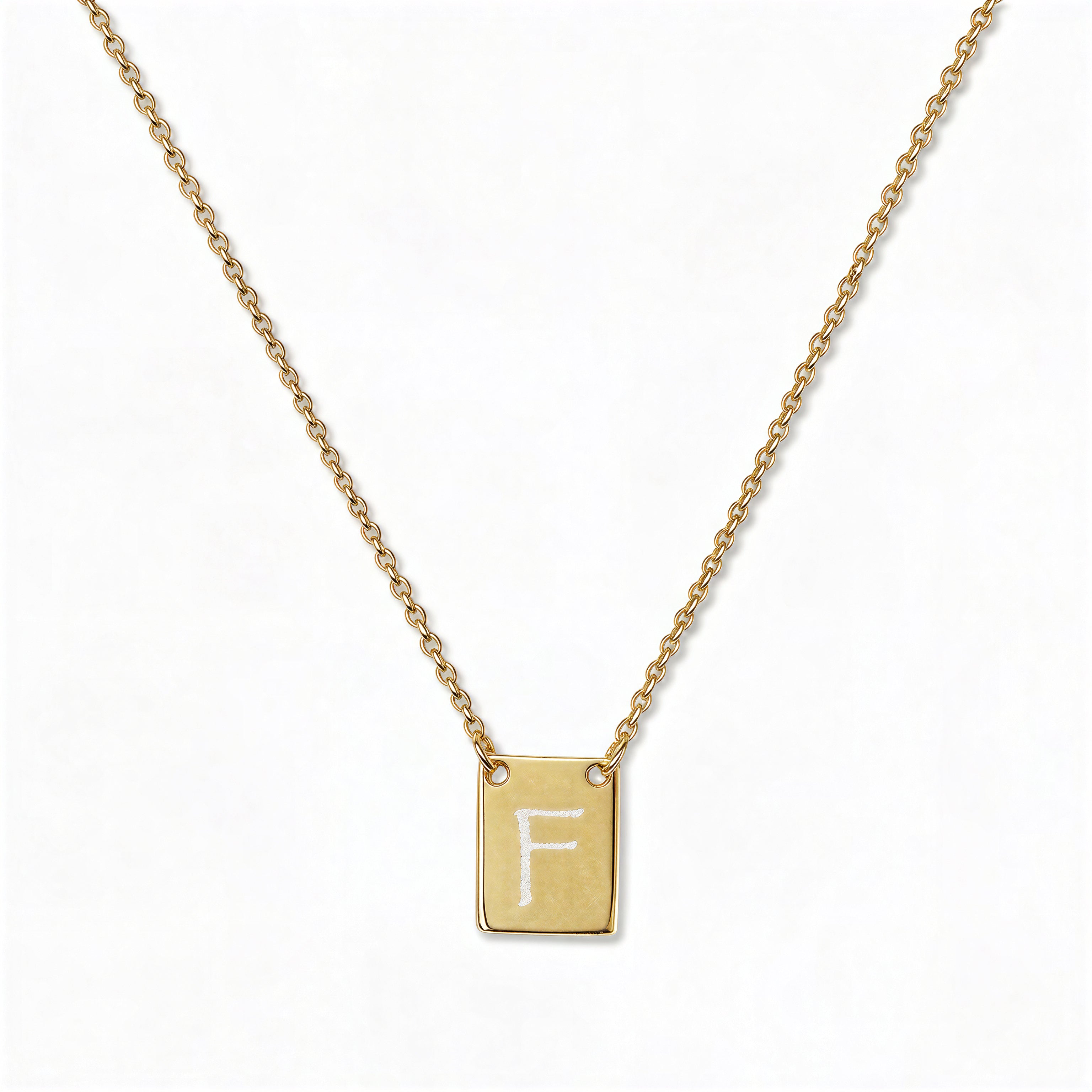 An Engraved Initial Necklace Letter F by Skōsh Jewelry, featuring a small rectangular tag engraved with the letter F on a fine gold chain, displayed against a white background.