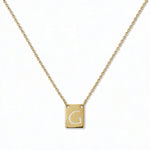 An Engraved Initial Necklace Letter G by Skōsh Jewelry, featuring a small rectangular tag engraved with the letter G on a fine gold chain, displayed against a white background.