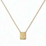 An Engraved Initial Necklace Letter G by Skōsh Jewelry, featuring a small rectangular tag engraved with the letter G on a fine gold chain, displayed against a white background.