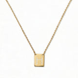 An Engraved Initial Necklace Letter H by Skōsh Jewelry, featuring a small rectangular tag engraved with the letter H on a fine gold chain, displayed against a white background.