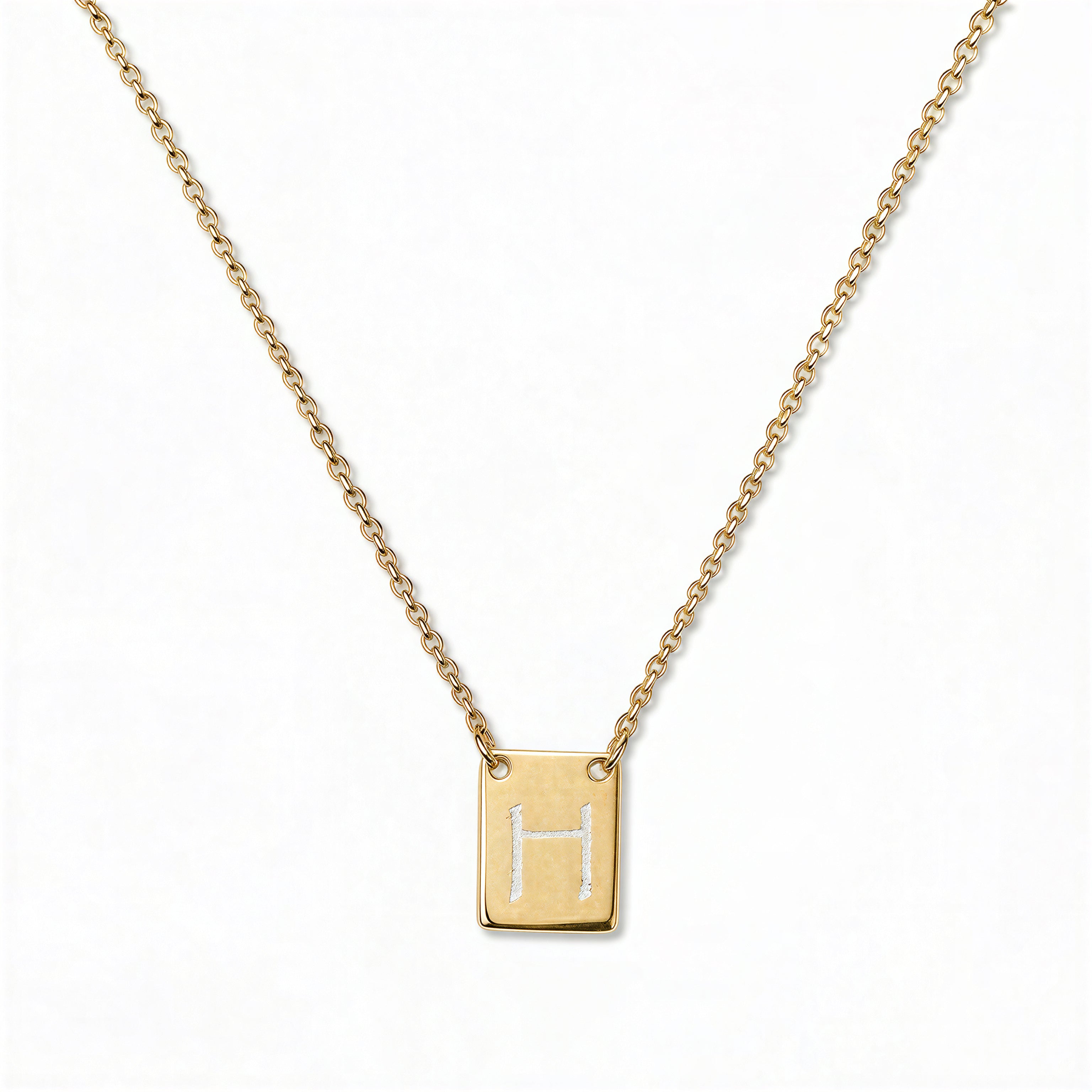 An Engraved Initial Necklace Letter H by Skōsh Jewelry, featuring a small rectangular tag engraved with the letter H on a fine gold chain, displayed against a white background.