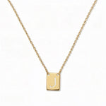 An Engraved Initial Necklace Letter J by Skōsh Jewelry, featuring a small rectangular tag engraved with the letter J on a fine gold chain, displayed against a white background.