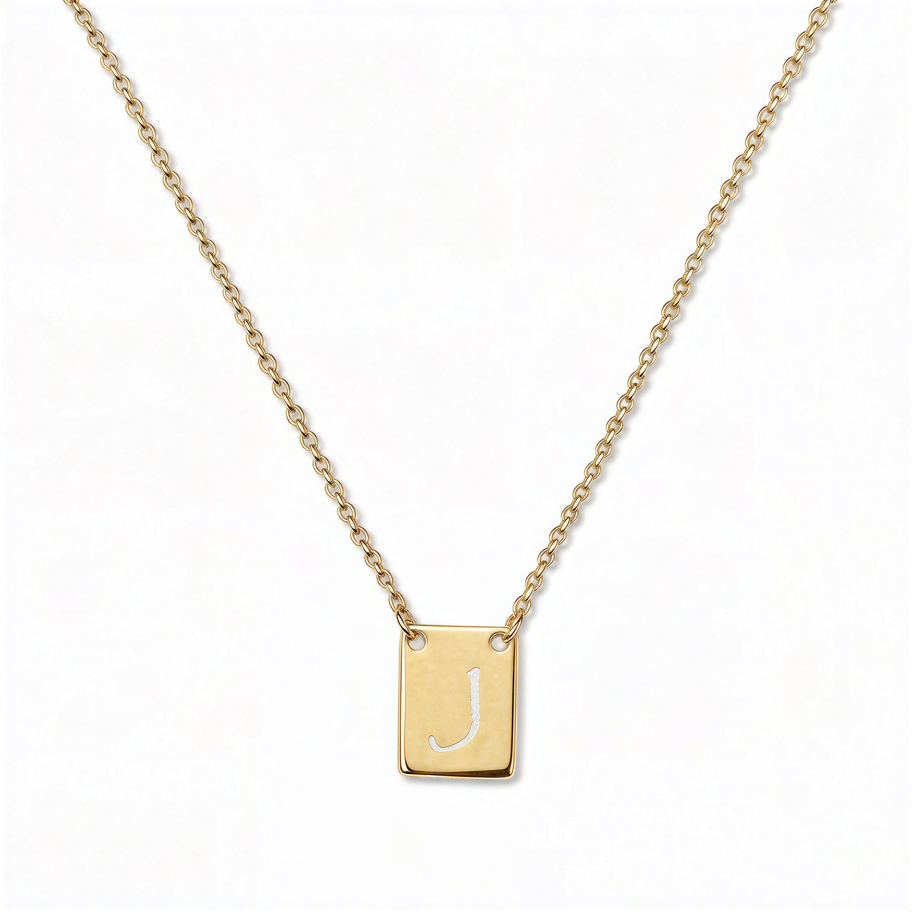 An Engraved Initial Necklace Letter J by Skōsh Jewelry, featuring a small rectangular tag engraved with the letter J on a fine gold chain, displayed against a white background.