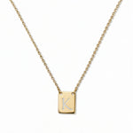 An Engraved Initial Necklace Letter K by Skōsh Jewelry, featuring a small rectangular tag engraved with the letter K on a fine gold chain, displayed against a white background.