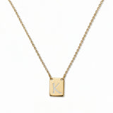 An Engraved Initial Necklace Letter K by Skōsh Jewelry, featuring a small rectangular tag engraved with the letter K on a fine gold chain, displayed against a white background.