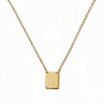 An Engraved Initial Necklace Letter L by Skōsh Jewelry, featuring a small rectangular tag engraved with the letter L on a fine gold chain, displayed against a white background.