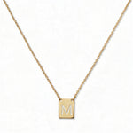 An Engraved Initial Necklace Letter M by Skōsh Jewelry, featuring a small rectangular tag engraved with the letter M on a fine gold chain, displayed against a white background.