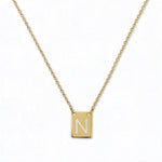 An Engraved Initial Necklace Letter N by Skōsh Jewelry, featuring a small rectangular tag engraved with the letter N on a fine gold chain, displayed against a white background.