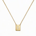 An Engraved Initial Necklace Letter R by Skōsh Jewelry, featuring a small rectangular tag engraved with the letter R on a fine gold chain, displayed against a white background.