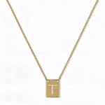An Engraved Initial Necklace Letter T by Skōsh Jewelry, featuring a small rectangular tag engraved with the letter T on a fine gold chain, displayed against a white background.